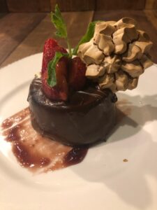 An irresistible dessert called the Chocolate Mousse Bomb, consisting of drunken strawberries, port wine reduction, and a meringue cookie.