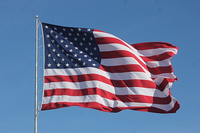 American flag waves in the wind in a blue sky. Photo by Noah Wulf.